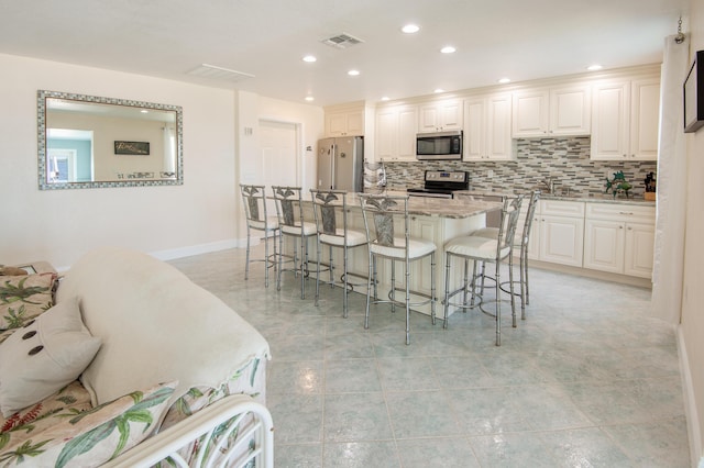 kitchen featuring a breakfast bar, light stone counters, tasteful backsplash, stainless steel appliances, and white cabinets