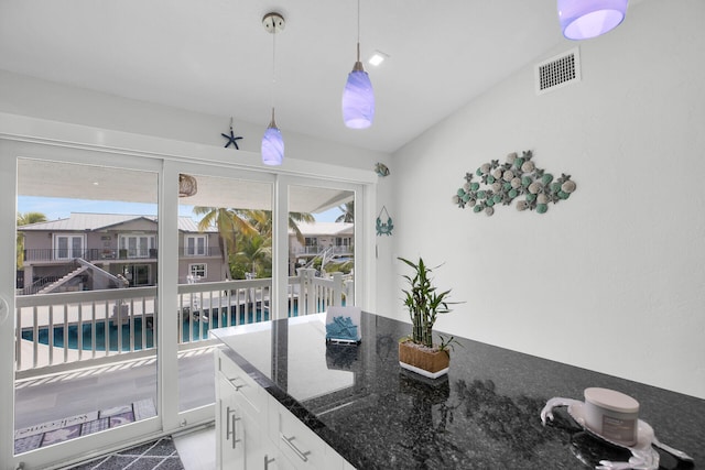 kitchen with white cabinetry, hanging light fixtures, and dark stone countertops