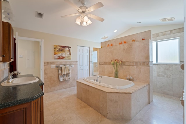 bathroom with lofted ceiling, ceiling fan, tile walls, vanity, and tiled bath