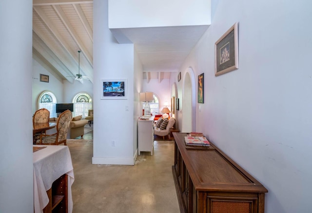 hallway with arched walkways, baseboards, and high vaulted ceiling