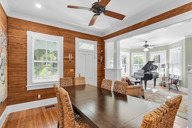 dining room with crown molding, wooden walls, and light hardwood / wood-style floors