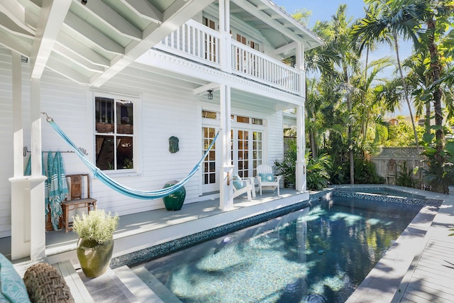 rear view of house with a swimming pool with hot tub, french doors, and a balcony