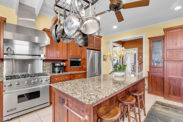 kitchen with a kitchen island, wall chimney range hood, premium appliances, and light tile patterned floors