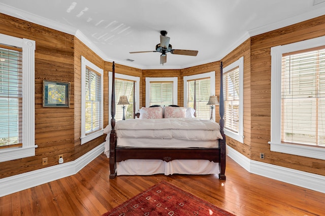 bedroom with multiple windows, crown molding, hardwood / wood-style flooring, and wood walls