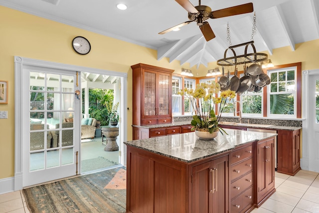 kitchen with light tile patterned flooring, lofted ceiling with beams, a kitchen island, stone counters, and ceiling fan