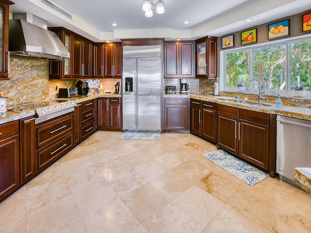 kitchen with sink, stainless steel appliances, tasteful backsplash, light stone countertops, and wall chimney exhaust hood