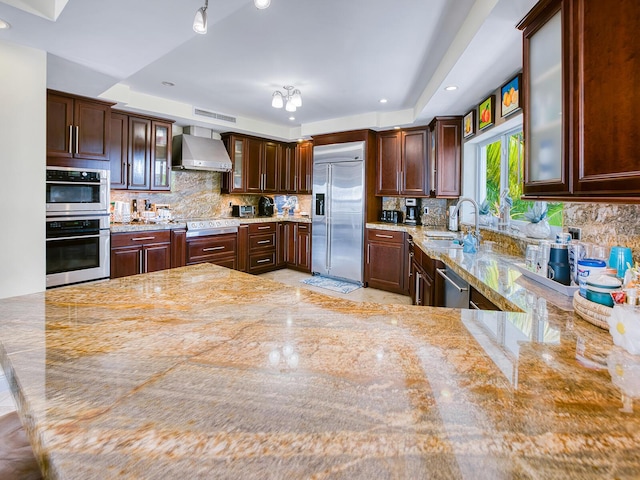 kitchen with wall chimney exhaust hood, appliances with stainless steel finishes, sink, and dark brown cabinets