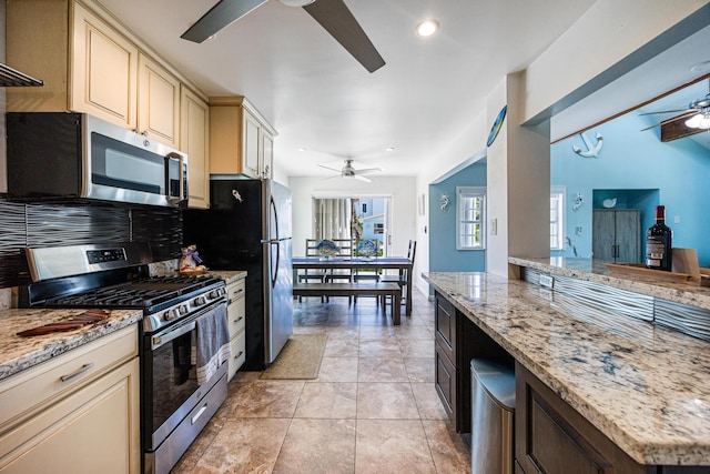 kitchen with light tile patterned floors, ceiling fan, stainless steel appliances, light stone countertops, and cream cabinetry