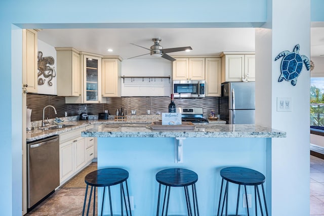 kitchen featuring sink, a breakfast bar area, stainless steel appliances, tasteful backsplash, and light stone countertops