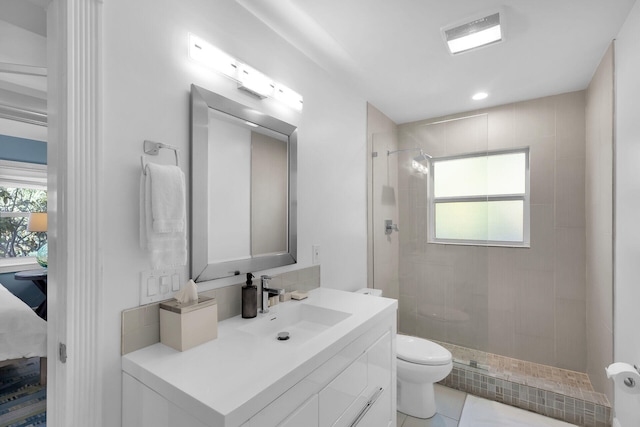 bathroom with vanity, a wealth of natural light, toilet, and tiled shower