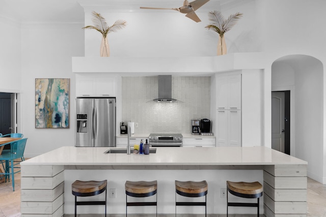 kitchen featuring wall chimney range hood, sink, a breakfast bar area, appliances with stainless steel finishes, and decorative backsplash