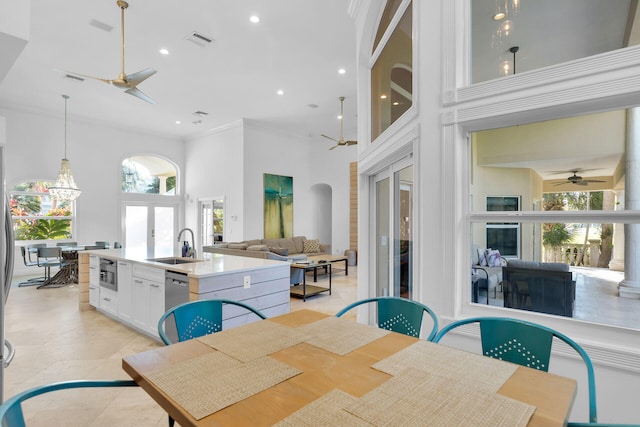 dining space featuring a towering ceiling, a wealth of natural light, sink, ornamental molding, and ceiling fan