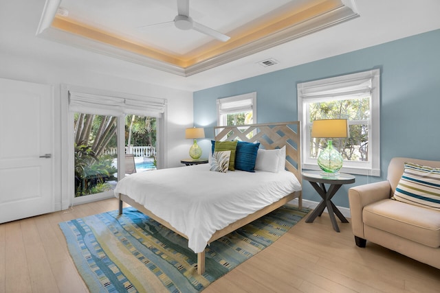 bedroom with access to exterior, a tray ceiling, light hardwood / wood-style flooring, and ornamental molding