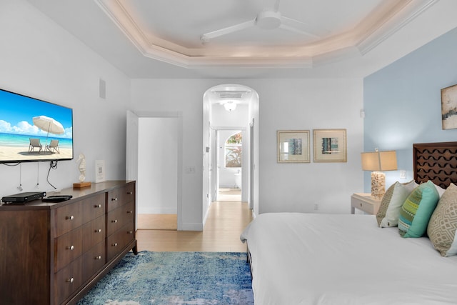 bedroom with ornamental molding, a raised ceiling, and light wood-type flooring