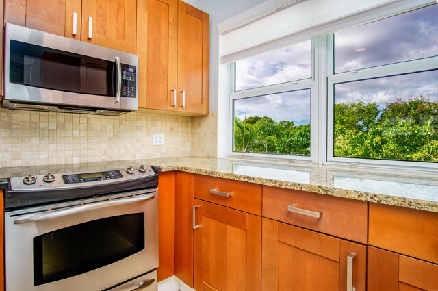 kitchen featuring light stone counters, backsplash, plenty of natural light, and appliances with stainless steel finishes