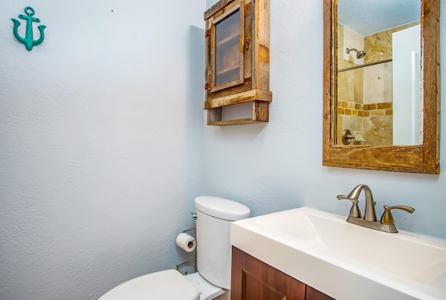 bathroom with vanity, toilet, and tiled shower