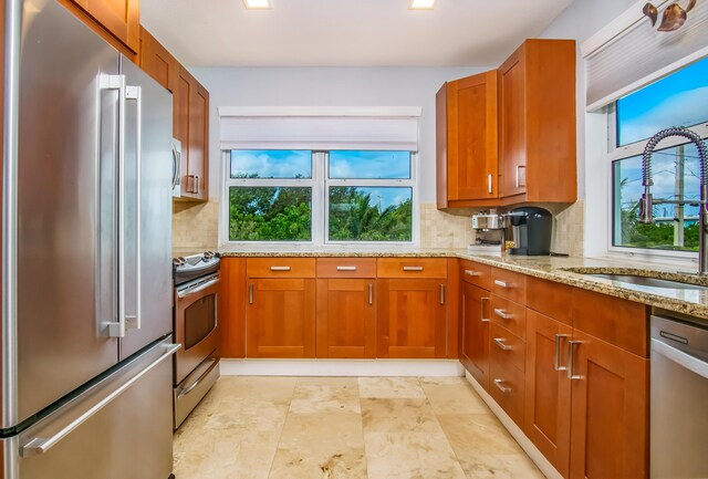 kitchen featuring light stone counters, stainless steel appliances, sink, and backsplash