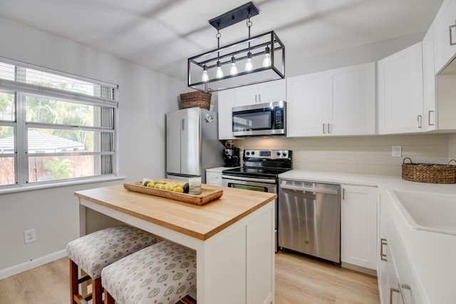 kitchen featuring a kitchen island, appliances with stainless steel finishes, wood counters, white cabinets, and a kitchen breakfast bar