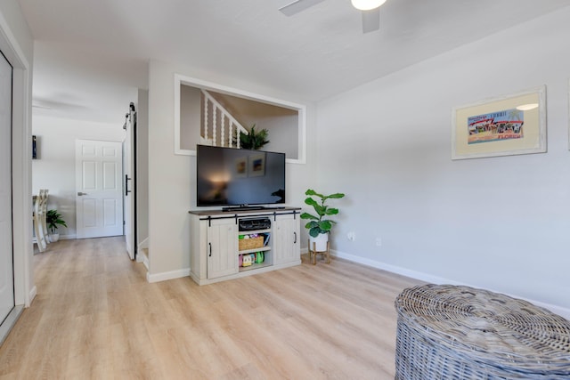 living room with ceiling fan, a barn door, and light hardwood / wood-style floors