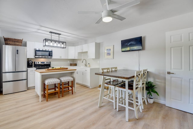 kitchen featuring sink, a breakfast bar, stainless steel appliances, white cabinets, and decorative light fixtures