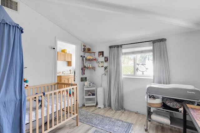 bedroom featuring lofted ceiling with beams, a nursery area, and light wood-type flooring