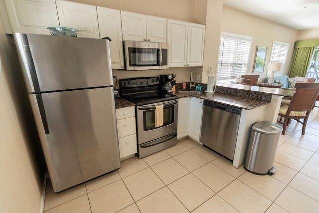 kitchen featuring dark stone countertops, light tile patterned floors, kitchen peninsula, stainless steel appliances, and white cabinets