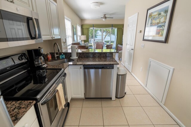 kitchen with appliances with stainless steel finishes, kitchen peninsula, dark stone counters, and white cabinets