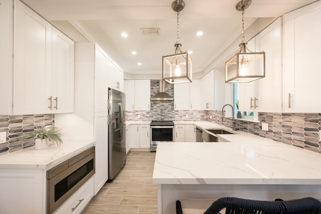 kitchen featuring appliances with stainless steel finishes, a sink, light stone countertops, a peninsula, and wall chimney exhaust hood