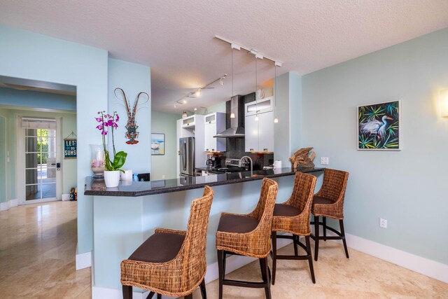 kitchen featuring white cabinets, a breakfast bar, kitchen peninsula, and wall chimney range hood