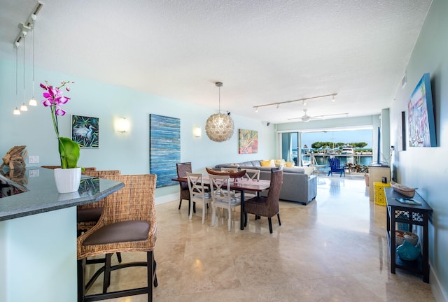 dining area featuring ceiling fan with notable chandelier, rail lighting, and a textured ceiling