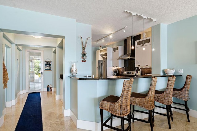 kitchen with a breakfast bar, stainless steel refrigerator, white cabinets, kitchen peninsula, and wall chimney range hood