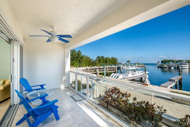 balcony with a water view, a dock, and ceiling fan