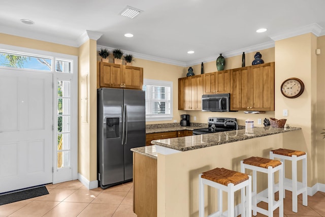 kitchen featuring appliances with stainless steel finishes, a kitchen bar, dark stone counters, ornamental molding, and kitchen peninsula