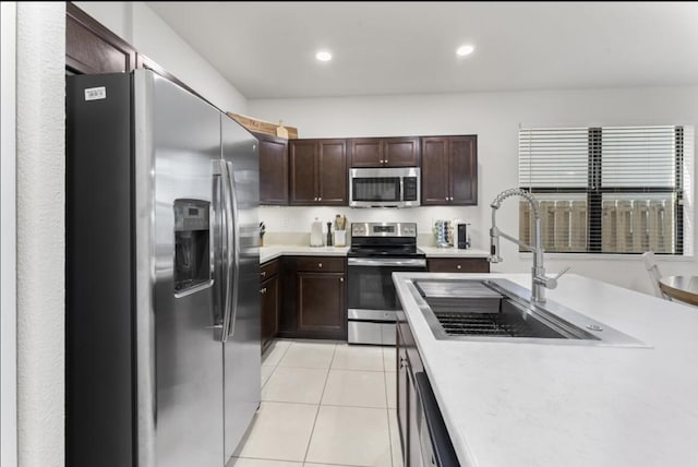 kitchen featuring sink, light tile patterned floors, dark brown cabinets, and stainless steel appliances