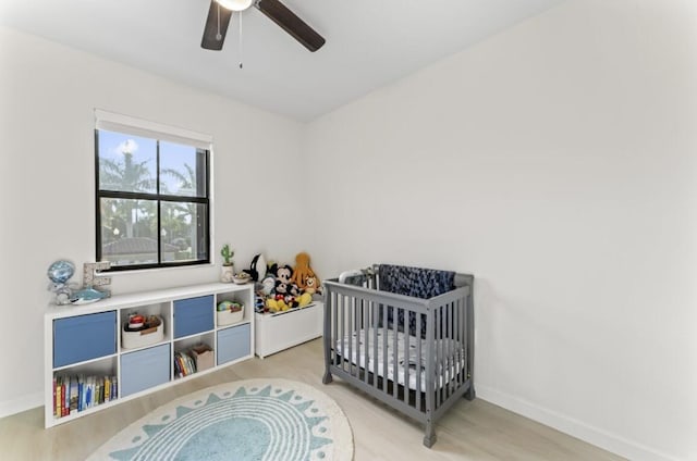 bedroom with hardwood / wood-style flooring, a nursery area, and ceiling fan