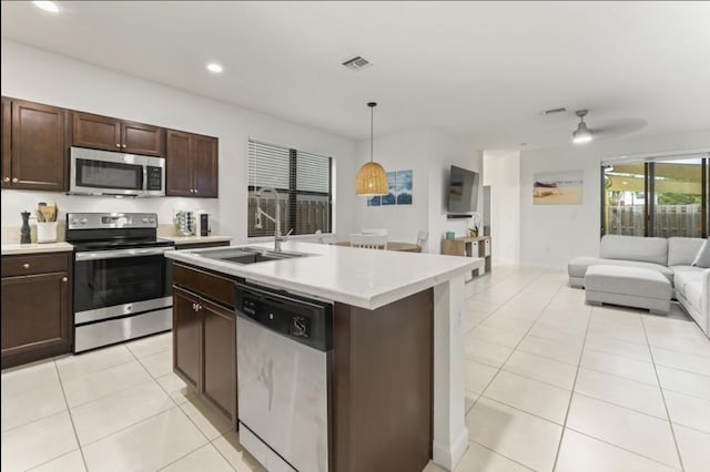 kitchen featuring light tile patterned flooring, appliances with stainless steel finishes, sink, hanging light fixtures, and a kitchen island with sink