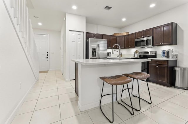 kitchen with appliances with stainless steel finishes, a breakfast bar, sink, a kitchen island with sink, and dark brown cabinets