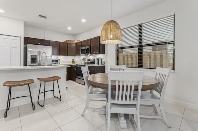 kitchen featuring dark brown cabinetry, hanging light fixtures, light tile patterned floors, and appliances with stainless steel finishes