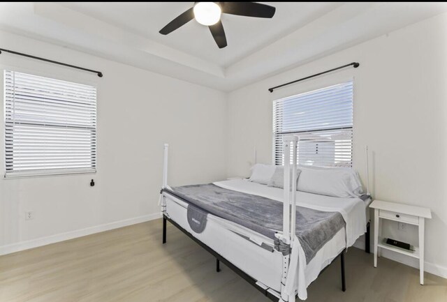 bedroom with a raised ceiling, ceiling fan, and light wood-type flooring