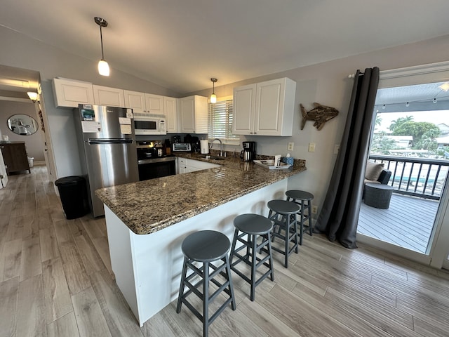 kitchen with stainless steel appliances, white cabinetry, vaulted ceiling, a sink, and a peninsula