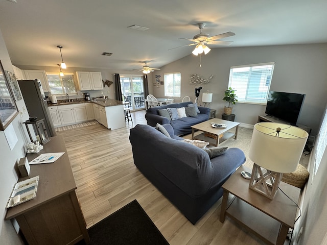 living room featuring plenty of natural light, light wood-type flooring, visible vents, and vaulted ceiling