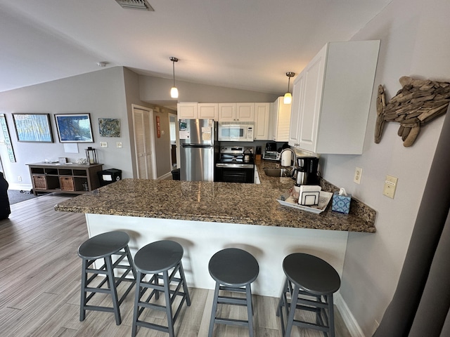 kitchen featuring light wood finished floors, stainless steel appliances, vaulted ceiling, a sink, and a peninsula