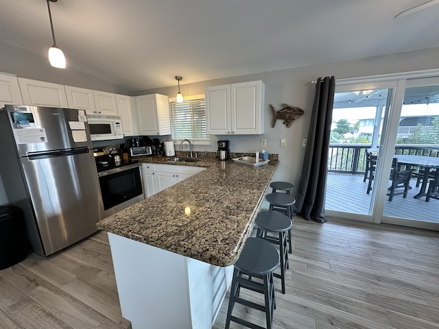 kitchen with white cabinets, appliances with stainless steel finishes, a peninsula, a healthy amount of sunlight, and a sink