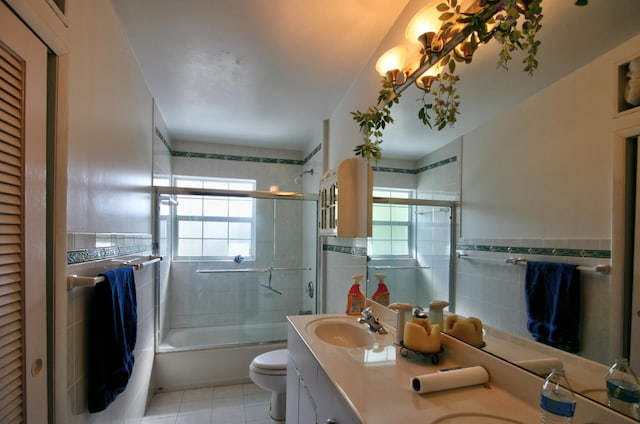 full bathroom with shower / bath combination with glass door, tile walls, vanity, tile patterned floors, and toilet