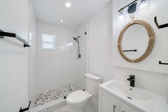 bathroom with a tile shower, vanity, and toilet