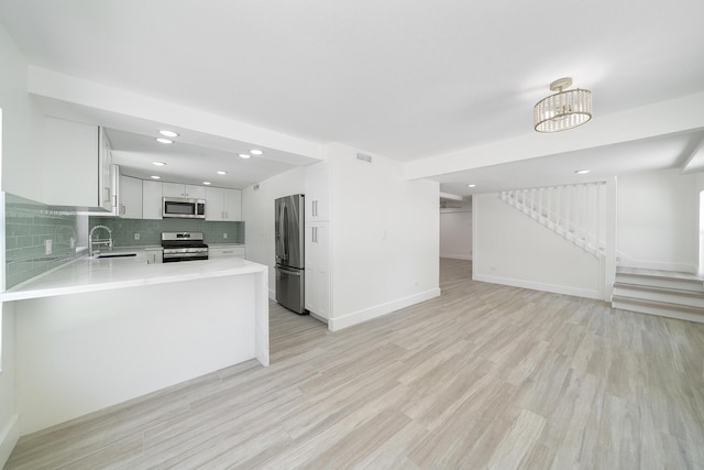 kitchen featuring white cabinets, appliances with stainless steel finishes, a peninsula, light countertops, and a sink