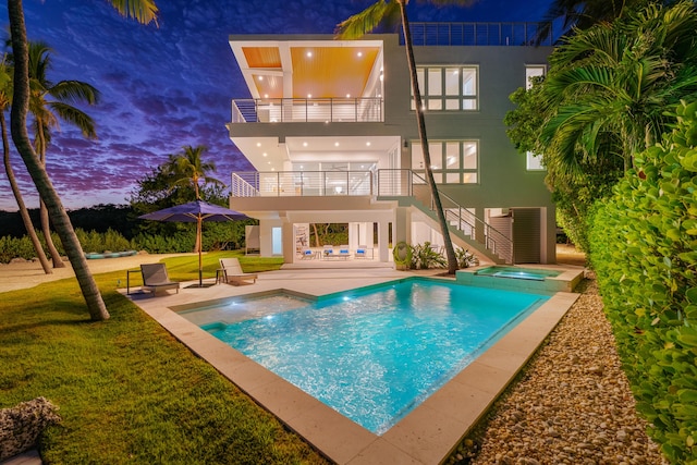 back house at dusk with a swimming pool with hot tub, a patio, and a lawn