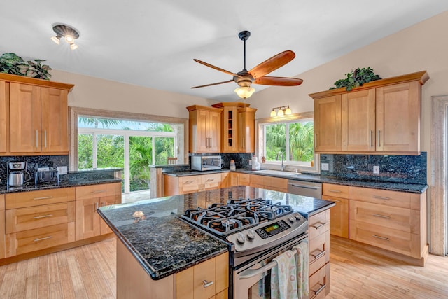 kitchen featuring sink, appliances with stainless steel finishes, dark stone countertops, a kitchen island, and light wood-type flooring