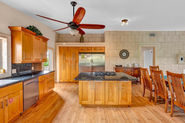 kitchen featuring stainless steel appliances, a center island, tasteful backsplash, light hardwood / wood-style floors, and dark stone counters