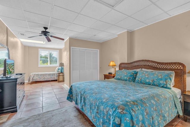 tiled bedroom with ceiling fan, a paneled ceiling, ornamental molding, and a closet